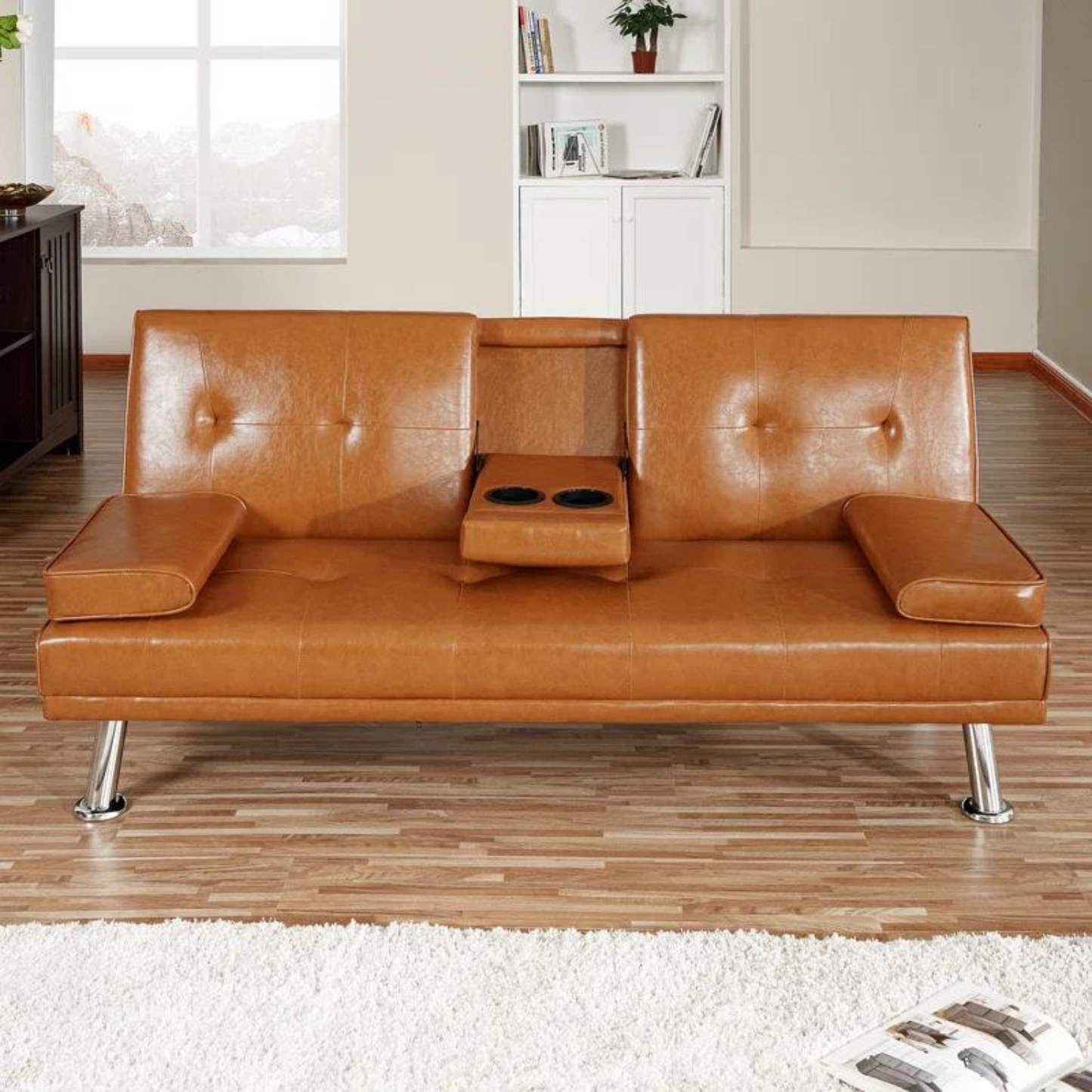 Couch Bed Futon Sleeper Sofa for Living Room | Tan Faux Leather from AHF Depot - Tan leather futon with center cupholders displayed against in a modern living room scene, offering a view out the window as well as to the bookshelf in the back. 