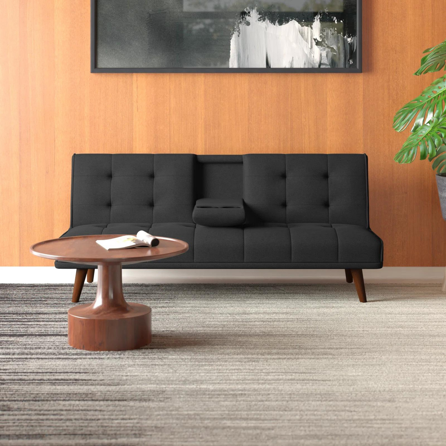 Couch Bed Futon Sleeper Sofa for Living Room | Black from AHF Depot - Black fabric futon with center cupholders displayed against a wooden wall backdrop in a modern living room scene, placed just behind a round wooden coffee table. 