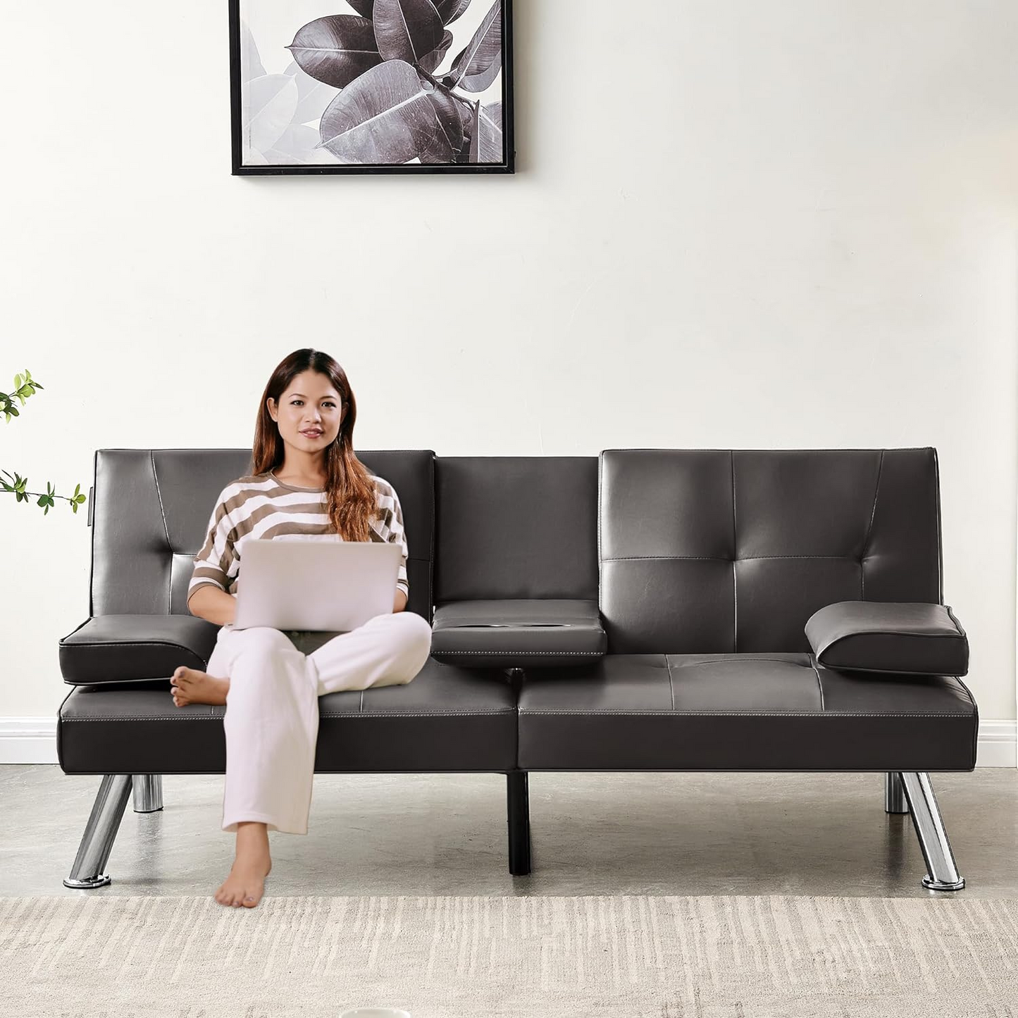 Couch Bed Futon Sleeper Sofa for Living Room | Brown Faux Leather from AHF Depot - Brown leather futon with center cupholders displayed in the couch position with a woman sitting on it in a light-toned modern living room scene against a clean wall.