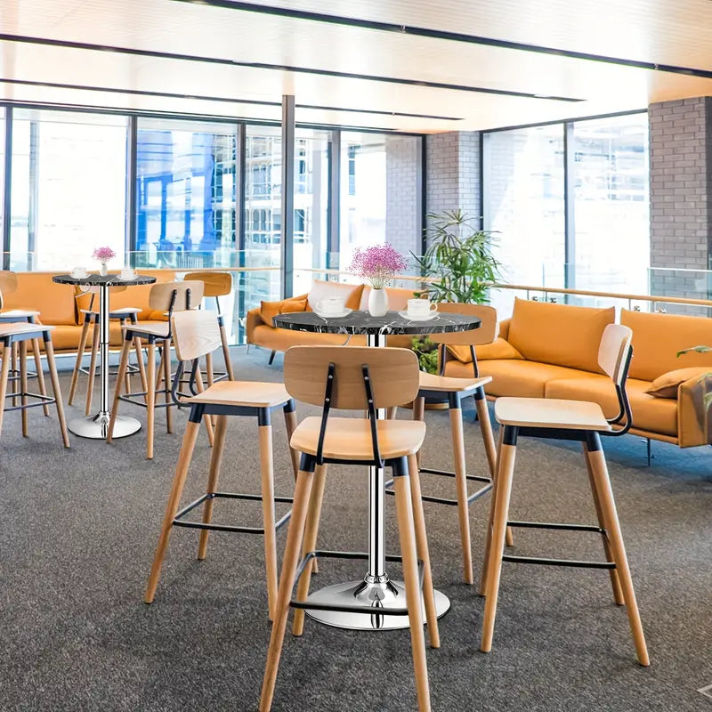 Bar Table Round with Adjustable Height and Swivel | Black from AHF Depot - Two modern black marble top bar tables with a sleek silver frame, each surrounded by four wooden chairs, in a vibrant college lounge scene.