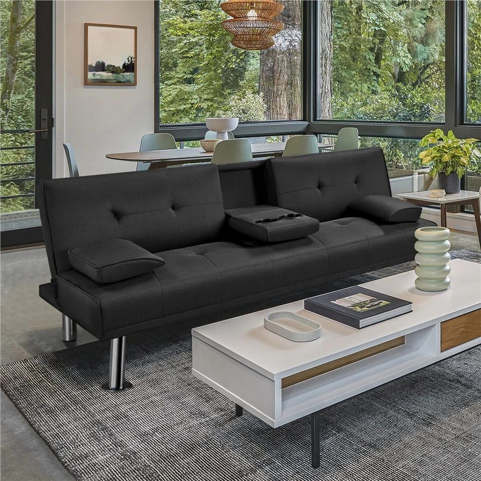 Couch Bed Futon Sleeper Sofa for Living Room | Black from AHF Depot - Black fabric futon with center cupholders displayed against bay windows in a modern living room scene, offering a view of lush greenery outside. 