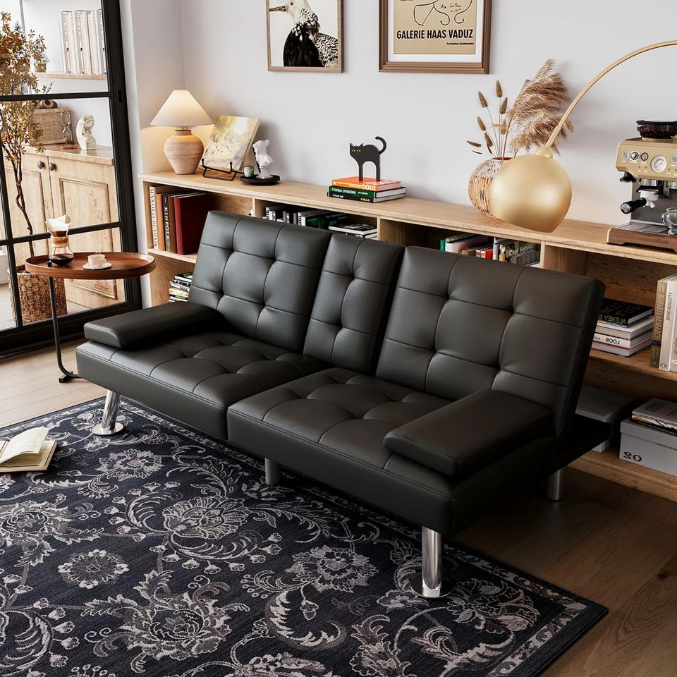 Couch Bed Futon Sleeper Sofa for Living Room | Black Faux Leather from AHF Depot - Black leather futon with center cupholders displayed against oak bookshelf in a modern living room scene, offering a view of various living room decor.