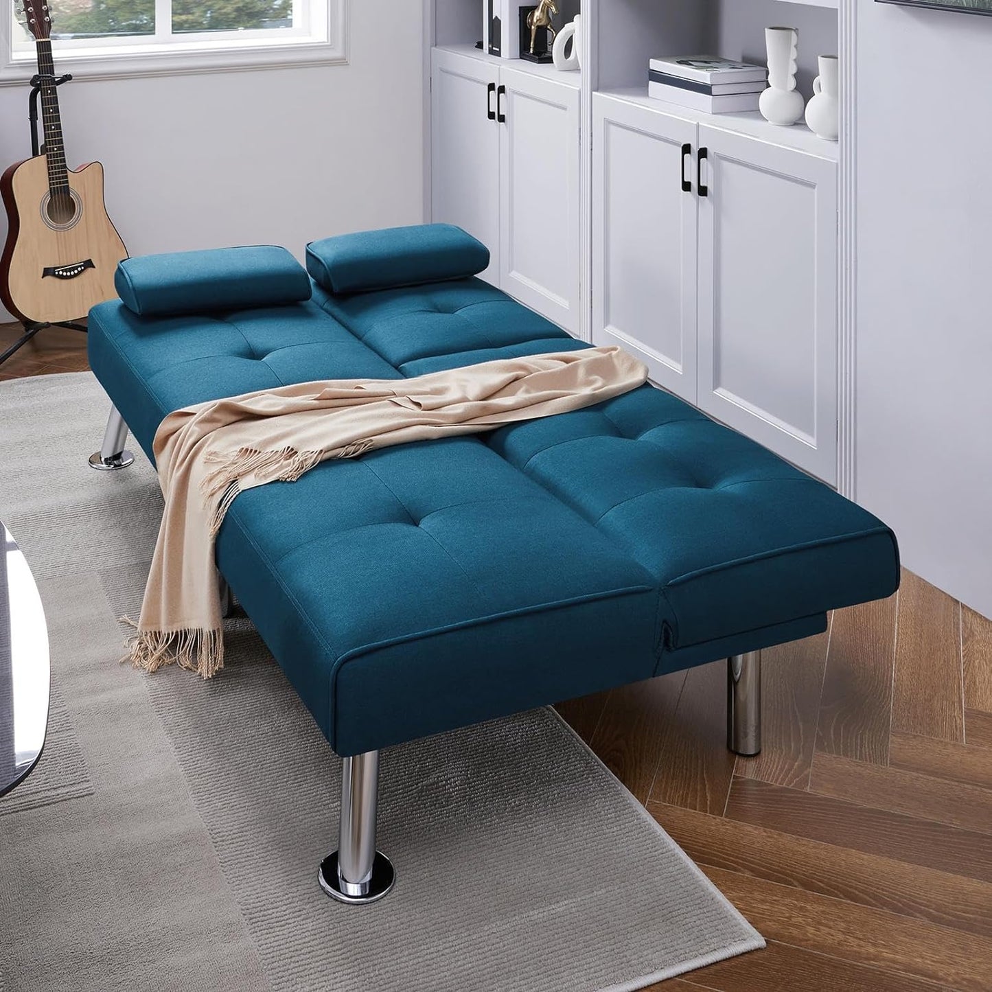 Couch Bed Futon Sleeper Sofa for Living Room | Blue from AHF Depot - blue fabric futon with center cupholders displayed in the bed position with a blanket on it in a white-washed modern bedroom scene.