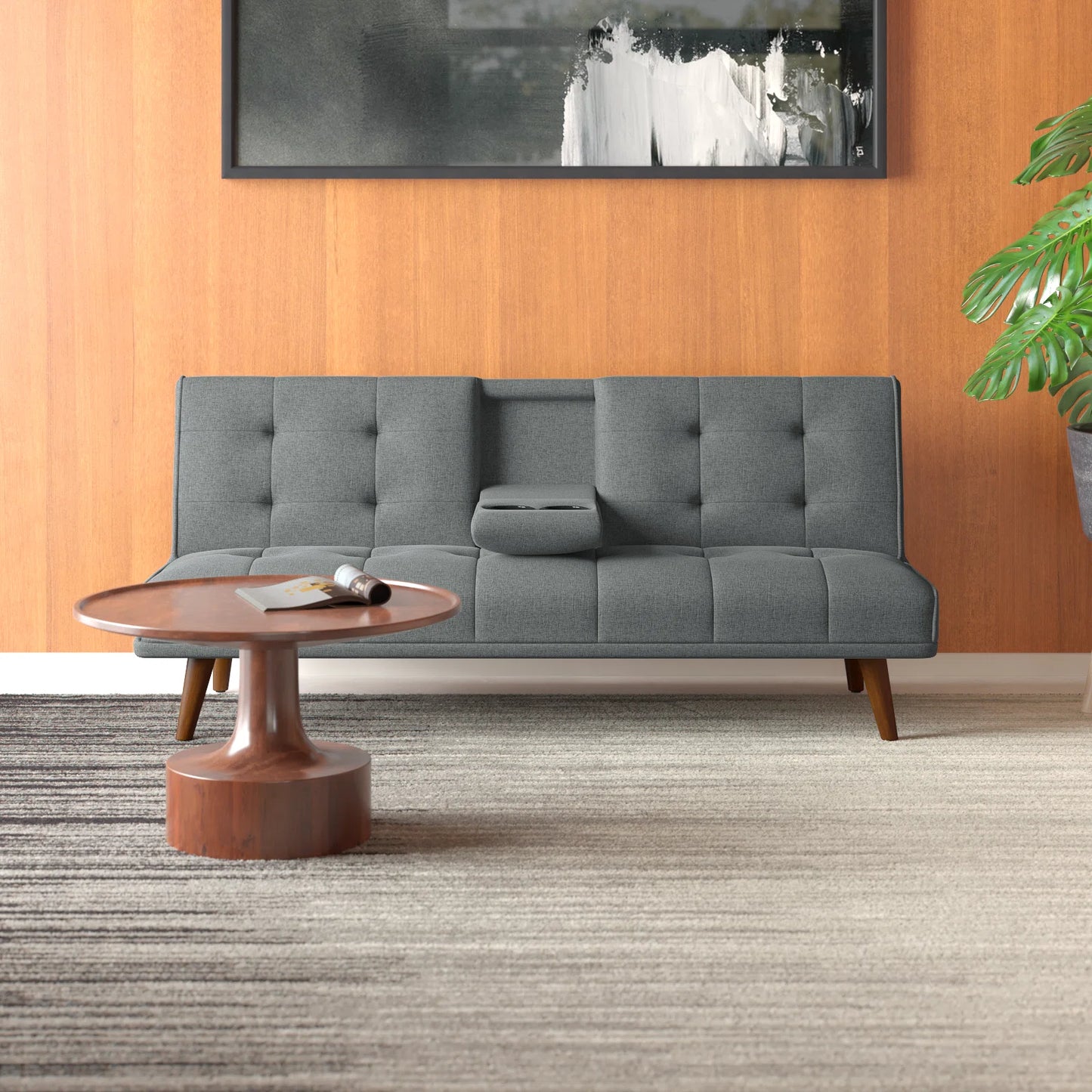 Couch Bed Futon Sleeper Sofa for Living Room | Grey from AHF Depot - Grey fabric futon with center cupholders displayed against a wooden wall backdrop in a modern living room scene, placed just behind a round wooden coffee table.