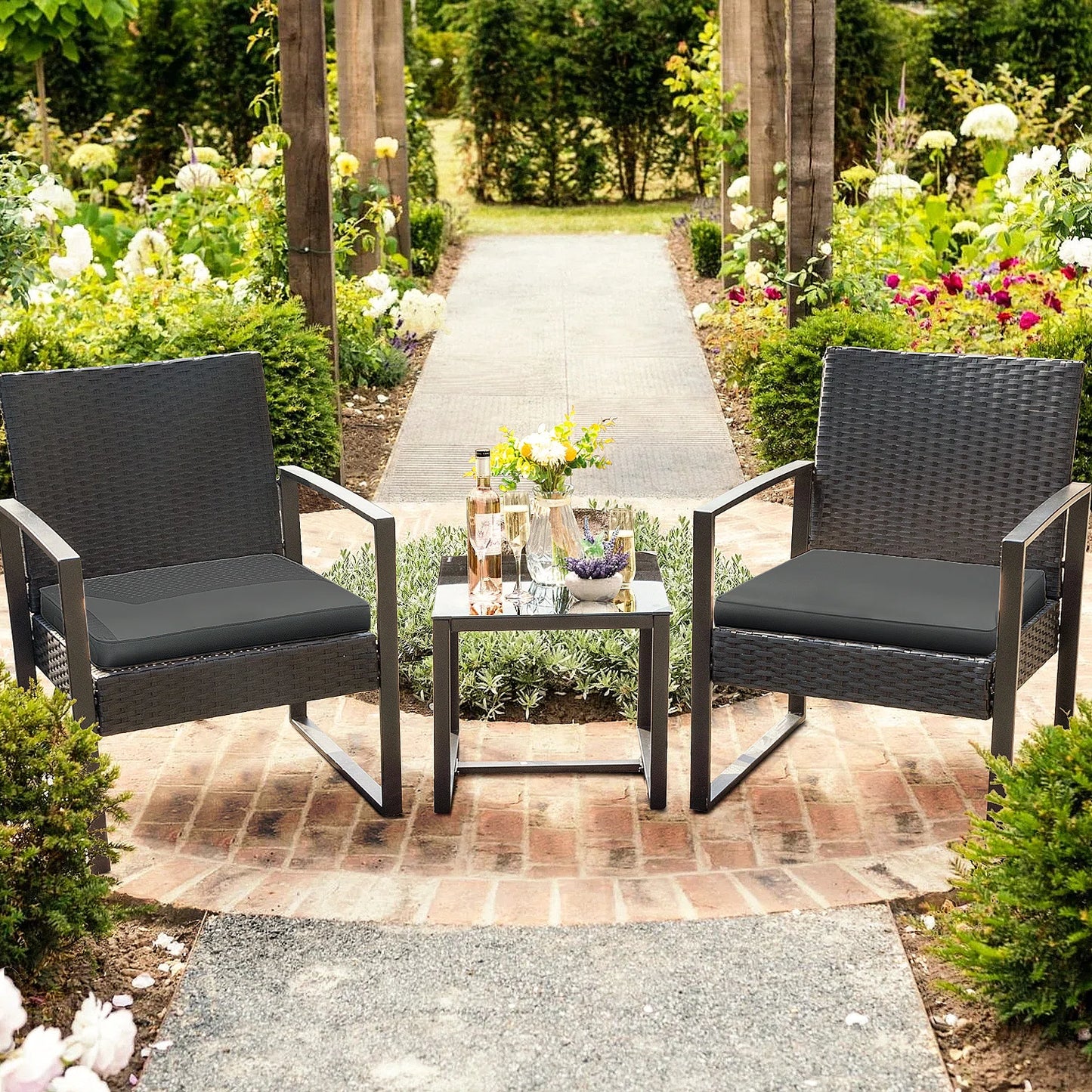 Outdoor Patio Chairs and Table Set | Black/Black from AHF Depot - Modern black frame patio conversation set with black cushions and small glass top table adorned with a bottle and glasses of wine, set amidst a sunny outdoor floral scene.