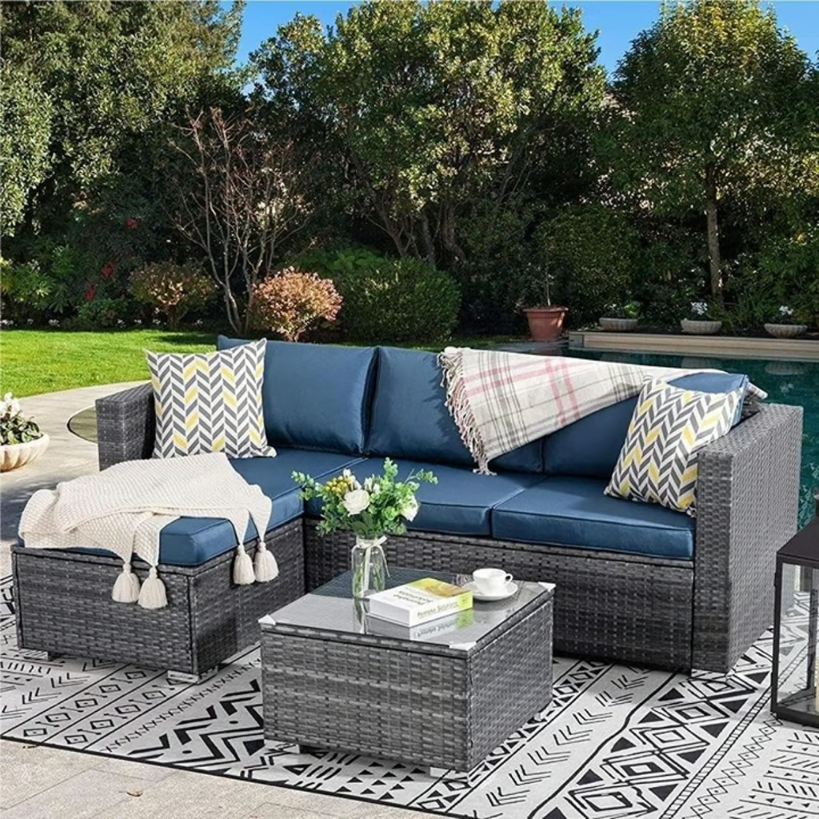 Outdoor Patio Sofa Set with Table | Grey/Blue from AHF Depot - Grey sectional couch with dark blue cushions and a small glass top table, complemented by a vase of flowers, set against a sunny poolside backdrop.