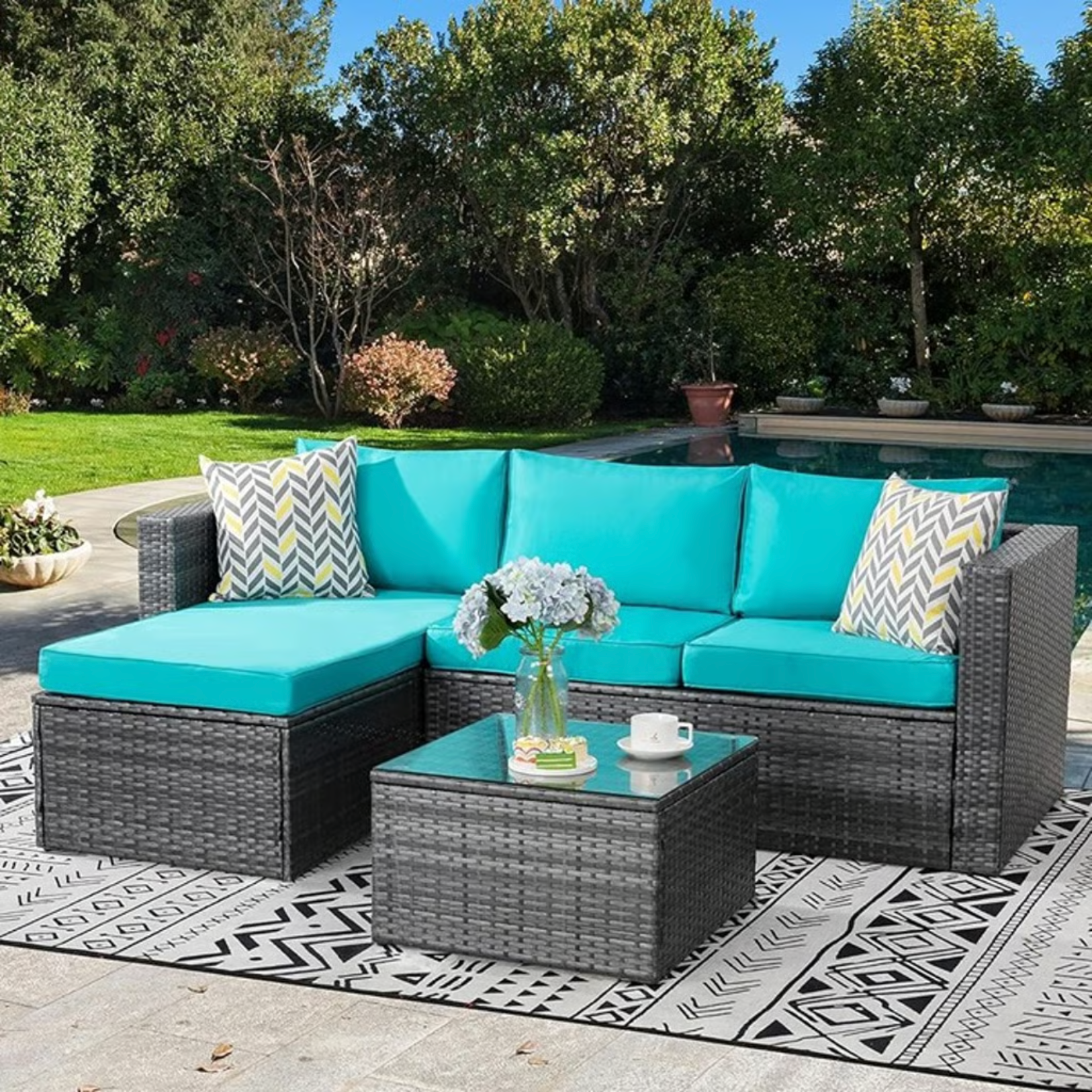 Outdoor Patio Sofa Set with Table | Grey/Teal from AHF Depot - Grey sectional couch with teal blue cushions and a small glass top table, complemented by a vase of flowers, set against a sunny poolside backdrop.